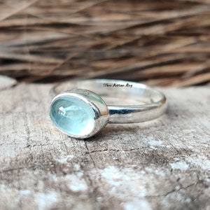 Puede incluir: Un anillo de plata con una piedra ovalada azul claro. El anillo est&aacute; colocado sobre una superficie de madera.