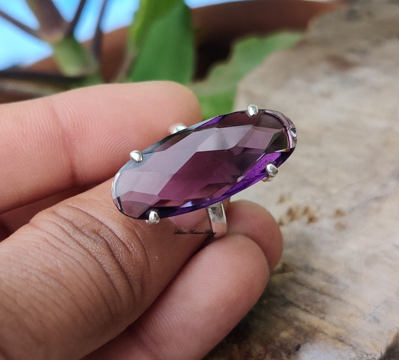 May include: A silver ring with a large, faceted, oval-shaped amethyst gemstone. The ring is set with small silver accents around the gemstone.