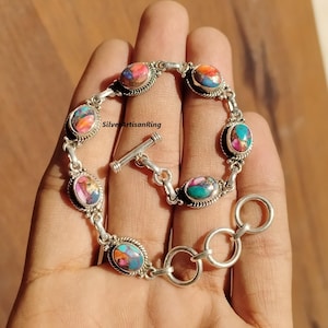 Pode incluir: Uma pulseira de prata com fecho de correr apresenta pedras ovais turquesa e rosa com detalhes intrincados em prata. A pulseira tem um design de elo de corrente.