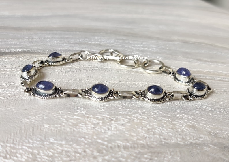 May include: A silver bracelet with a chain link design and six oval-shaped blue gemstones.