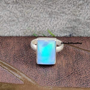 May include: A silver ring with a rectangular blue opal gemstone. The ring is on a brown leather surface.