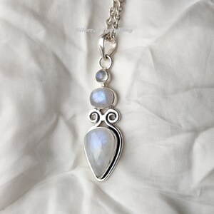 May include: A silver pendant with three moonstone gems. The pendant is in the shape of a teardrop with a smaller round moonstone above it and a smaller round moonstone above that. The pendant is on a silver chain.