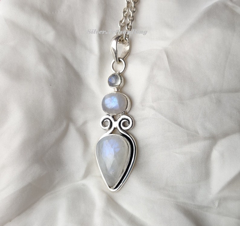 May include: A silver pendant with three moonstone gems. The pendant is in the shape of a teardrop with a smaller round moonstone above it and a smaller round moonstone above that. The pendant is on a silver chain.