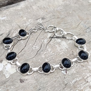 May include: A silver bracelet with black oval gemstones. The bracelet has a toggle clasp.