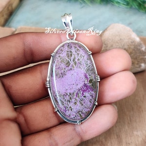 May include: A silver pendant with a large oval-shaped purple and green stone. The stone has a unique pattern of veins and swirls.