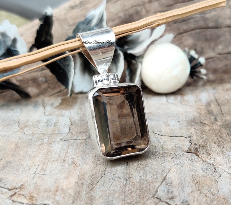 Pode incluir: Um pingente de prata com uma pedra preciosa de quartzo fumado marrom. O pingente tem formato retangular e um acabamento liso e polido. A pedra preciosa est&aacute; engastada em um bezel de prata e tem um brilho sutil.
