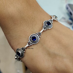 Könnte beinhalten: Ein silbernes Armband mit blauen Edelsteinen, die in verzierten Silberkreisen gefasst sind. Das Armband befindet sich an einem Handgelenk.