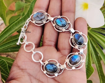 May include: A silver bracelet with five oval-shaped labradorite gemstones. Each gemstone is set in a silver frame with a decorative design. The bracelet has a toggle clasp.