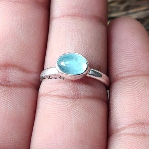 Puede incluir: Un anillo de plata con una piedra ovalada azul claro. El anillo est&aacute; en un dedo.
