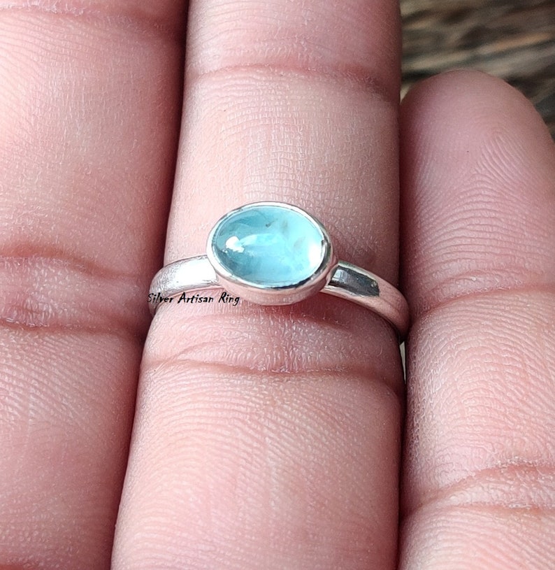 Puede incluir: Un anillo de plata con una piedra ovalada azul claro. El anillo est&aacute; en un dedo.