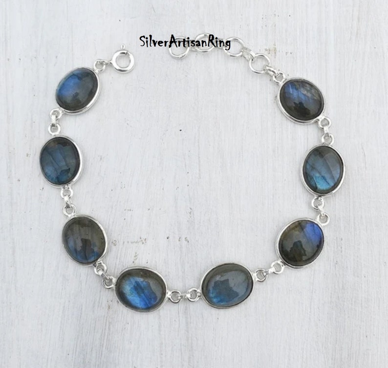 May include: A silver bracelet with a chain link design and oval-shaped labradorite gemstones. The stones have a dark blue and green iridescent sheen.