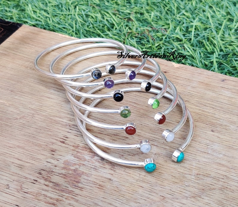 Pode incluir: Um conjunto de oito pulseiras de prata, cada uma com uma gema de cor diferente. As pulseiras t&ecirc;m um design simples e curvo, com uma &uacute;nica gema na extremidade. As gemas s&atilde;o pretas, ametistas, verdes, vermelhas, brancas e turquesas.