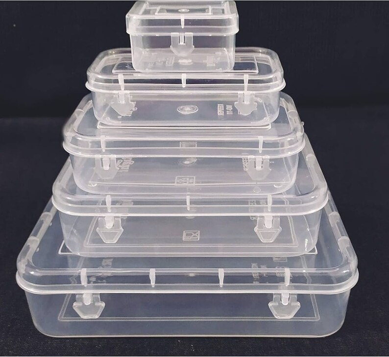 Op de afbeelding: Set van vijf doorzichtige plastic opbergdozen met deksels. De dozen zijn op elkaar gestapeld, met de grootste doos onderaan en de kleinste doos bovenaan.