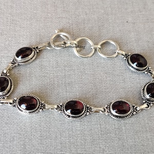 May include: A silver bracelet with a chain link design and six oval-shaped red gemstones. The bracelet has a lobster claw clasp.