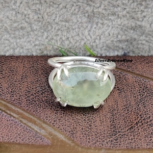 May include: A silver ring with a green gemstone. The ring has a claw setting and the gemstone is oval shaped.