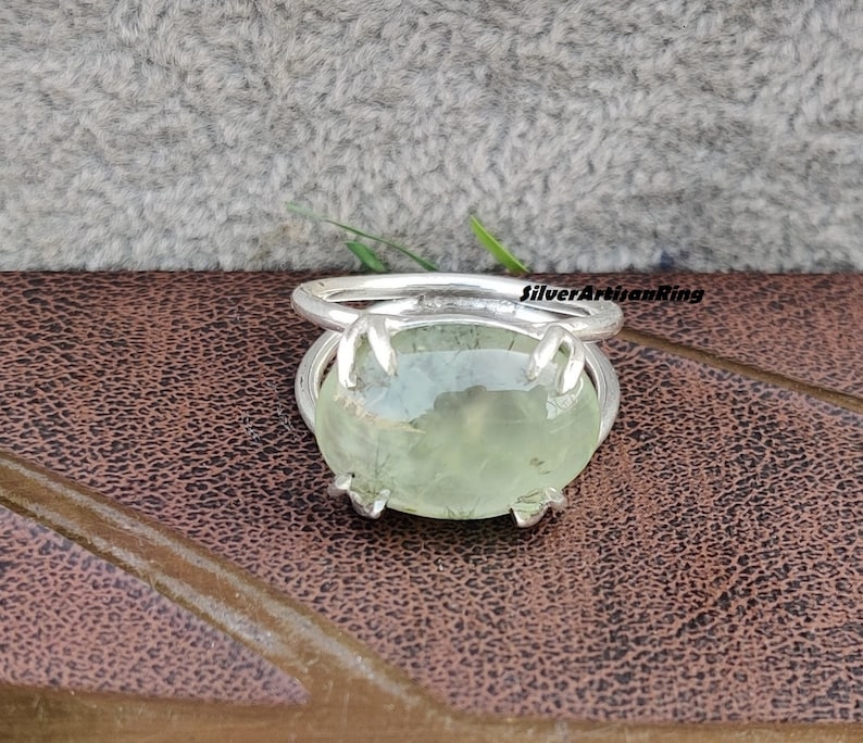 May include: A silver ring with a green gemstone. The ring has a claw setting and the gemstone is oval shaped.