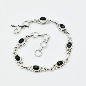 Könnte beinhalten: Ein silbernes Armband mit einem Gliederketten-Design und sechs schwarzen ovalen Edelsteinen. Das Armband hat einen Karabinerverschluss.
