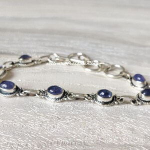 May include: A silver bracelet with a chain link design and oval-shaped purple gemstones. The bracelet has a clasp closure.