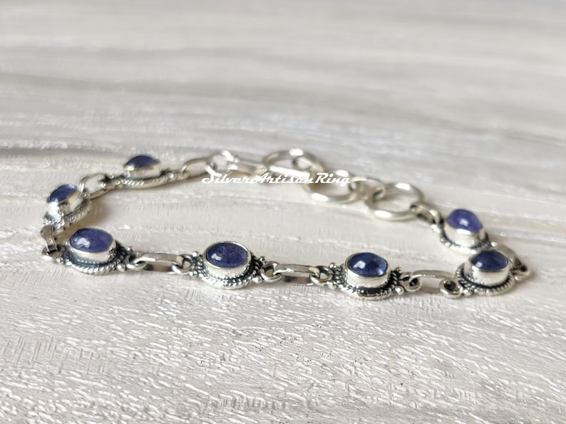 May include: A silver bracelet with a chain link design and oval-shaped purple gemstones. The bracelet has a clasp closure.