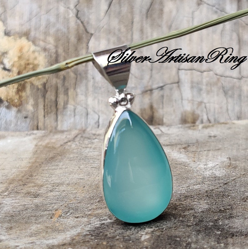 May include: A teardrop-shaped pendant with a light blue gemstone set in silver. The pendant is hanging from a silver chain.