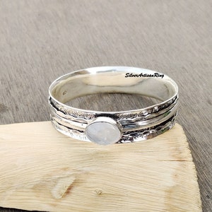 Op de afbeelding: Een zilveren ring met een witte maansteen in het midden. De ring heeft een gehamerde textuur en is gemaakt van meerdere banden.
