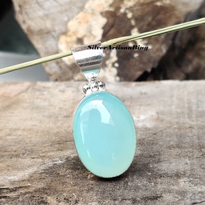 May include: A silver pendant with an oval, light blue gemstone. The gemstone is set in a silver bezel and has a smooth, polished surface. The pendant has a simple, elegant design, suitable for everyday wear.