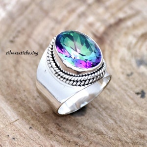 May include: A silver ring with a large, oval-shaped, iridescent gemstone set in a silver band with a rope-like design. The gemstone has shades of green, blue, and purple.