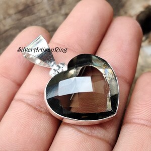 May include: A silver heart-shaped pendant with a clear smoky quartz gemstone. The pendant is on a silver chain.