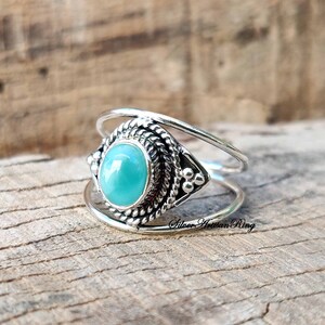 Pu&ograve; includere: Un anello d'argento con una pietra turchese incastonata in una montatura d'argento dettagliata. L'anello ha un design a doppia fascia.