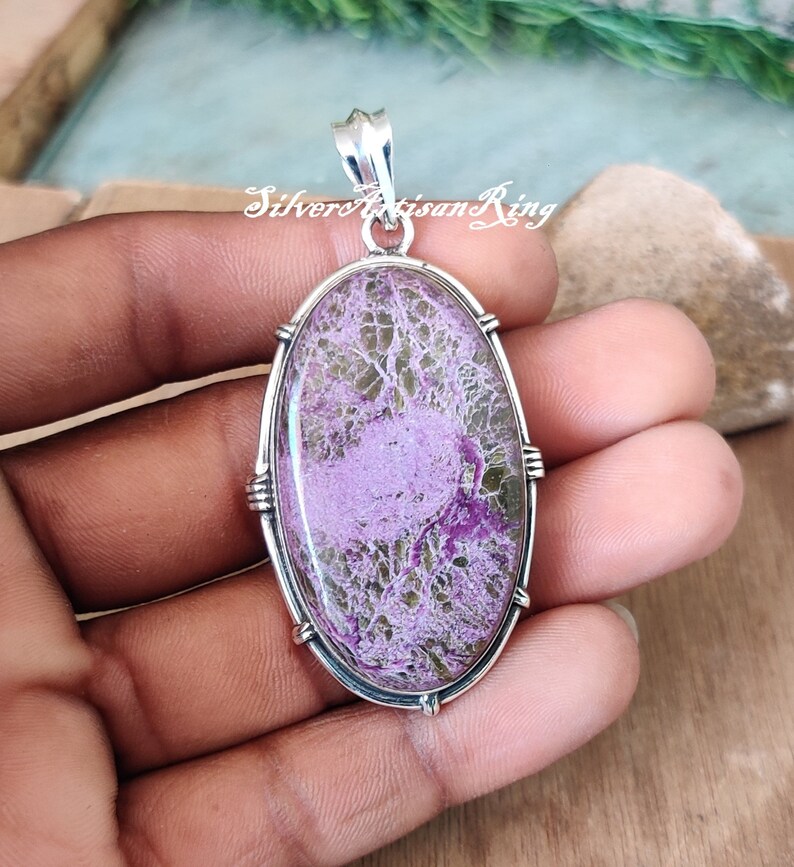 May include: A silver pendant with a large oval-shaped purple and green stone set in a silver bezel. The stone has a unique, swirling pattern.