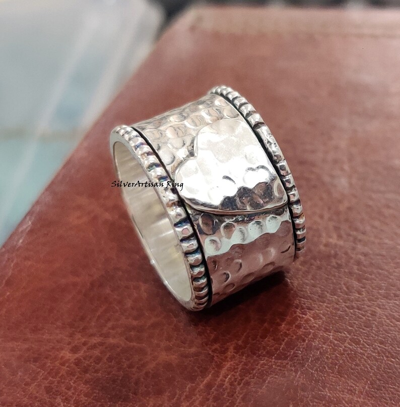 Pu&ograve; includere: Un anello girevole in argento con finitura martellata e un design a forma di cuore. L'anello ha un bordo perlato.
