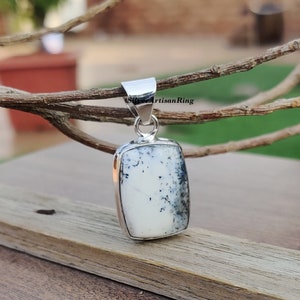 Puede incluir: Un colgante de plata con una piedra de ágata dendrítica blanca y negra. La piedra es rectangular y tiene un acabado liso y pulido.