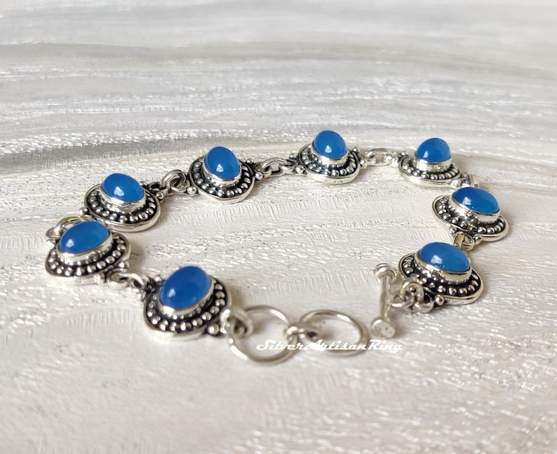 May include: A silver bracelet with blue gemstone accents. The bracelet has a toggle clasp.