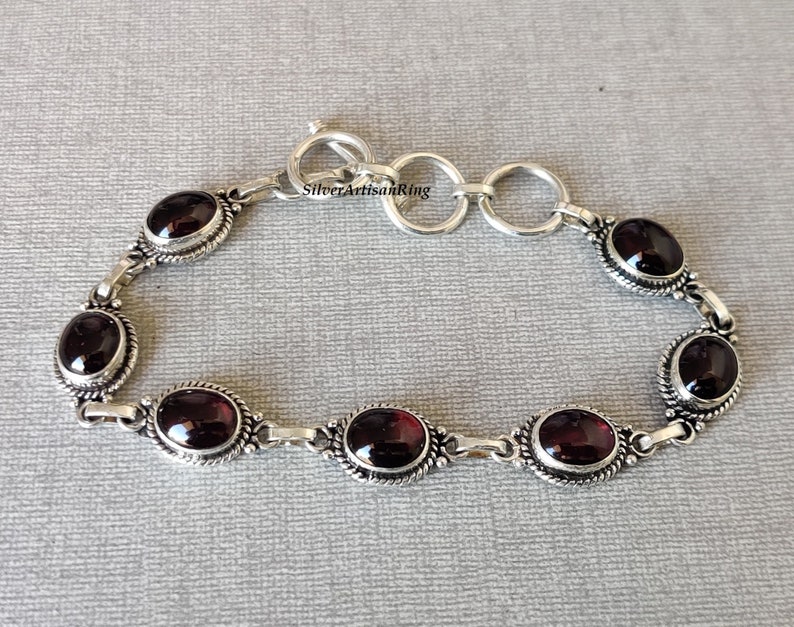 May include: A silver bracelet with a chain link design and six oval-shaped red gemstones. The bracelet has a lobster claw clasp.
