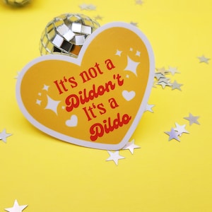 May include: A yellow heart-shaped sticker with the text "It's not a Dildo'n't It's a Dildo" in red and white lettering.