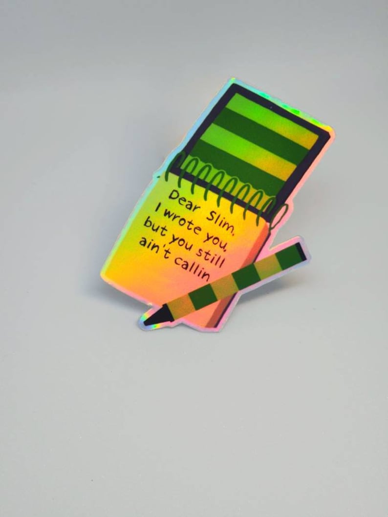 Puede incluir: Pegatina hologr&aacute;fica con un dise&ntilde;o de bloc de notas y l&aacute;piz. El bloc de notas tiene rayas verdes y amarillas y el texto "Dear Slim, I wrote you, but you still ain't callin". El l&aacute;piz es verde y marr&oacute;n.