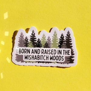 May include: A white sticker with a green and black illustration of a forest and the text "Born and raised in the Wishabitch Woods".