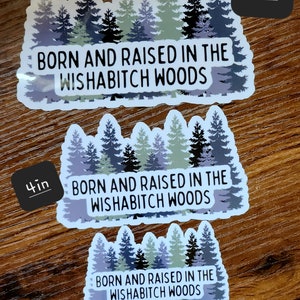 May include: Three different sizes of stickers featuring a forest scene with the text "Born and Raised in the Wishabitch Woods". The stickers are 3 inches, 4 inches, and 5 inches in size.