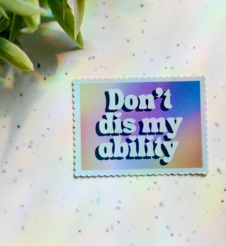 May include: A rectangular sticker with a scalloped edge features the text "Don't dis my ability" in white, bold font. The background has a gradient of pink, purple, and blue hues. The sticker is on a white surface.