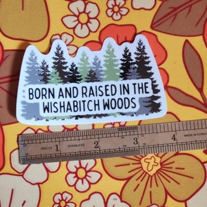 May include: White sticker with a green, black, and gray silhouette of a forest with the text "BORN AND RAISED IN THE WISHABITCH WOODS".