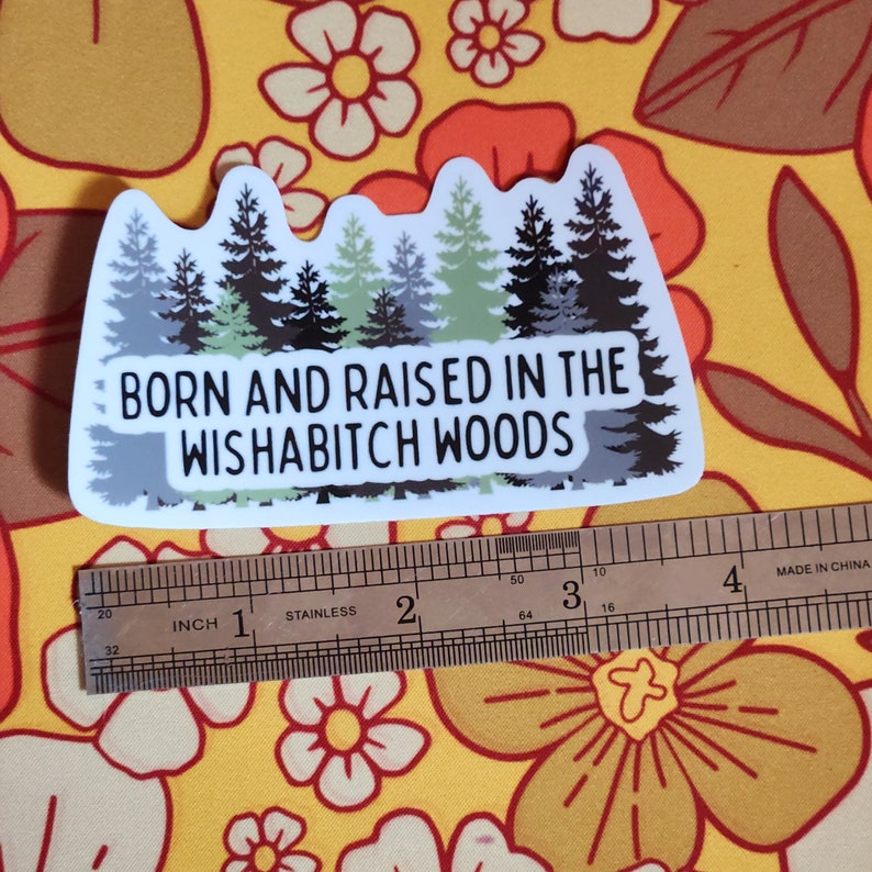 May include: White sticker with a green, black, and gray silhouette of a forest with the text "BORN AND RAISED IN THE WISHABITCH WOODS".