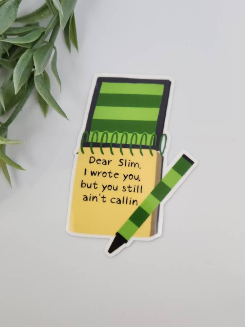 Puede incluir: Una pegatina con un bloc de notas amarillo con el texto "Dear Slim, I wrote you, but you still ain't callin" y un l&aacute;piz verde y negro. El bloc de notas tiene una cubierta a rayas verdes y una encuadernaci&oacute;n en espiral.