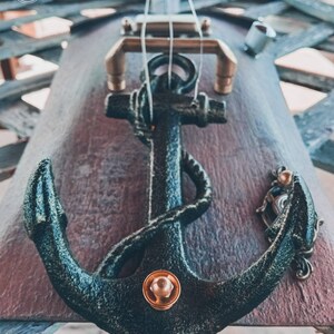 May include: A close-up of a black anchor with a gold accent on a wooden surface. The anchor is a decorative element on a musical instrument.