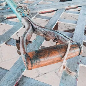 May include: A repurposed garden tool transformed into a unique musical instrument. The tool is made of wood and metal, with a blue and green paint finish. It has strings and tuning pegs, and a wooden handle.