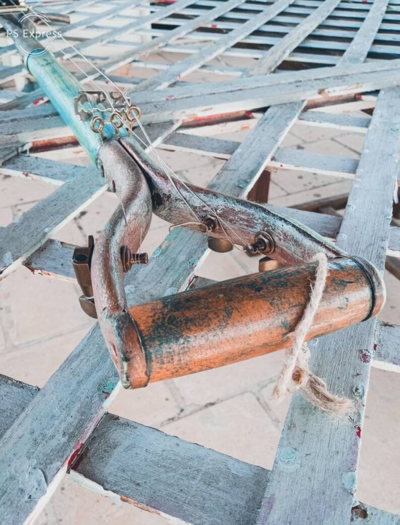 May include: A repurposed garden tool transformed into a unique musical instrument. The tool is made of wood and metal, with a blue and green paint finish. It has strings and tuning pegs, and a wooden handle.