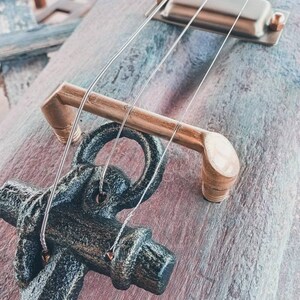 May include: A close-up of a wooden guitar with a black anchor as the bridge. The guitar has a brass tuning peg and a silver pickup.