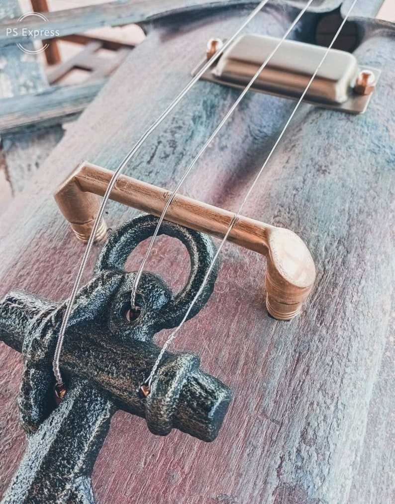 May include: A close-up of a wooden guitar with a black anchor as the bridge. The guitar has a brass tuning peg and a silver pickup.