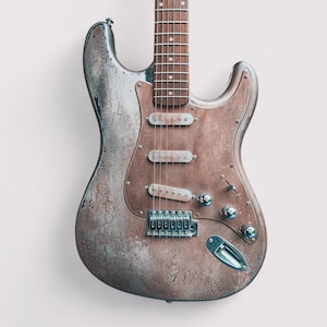 Könnte beinhalten: Eine Vintage-E-Gitarre mit einem abgenutzten, verwitterten Finish. Die Gitarre hat einen hellbraunen Korpus mit einem silbernen Schlagbrett und verchromten Hardware. Die Gitarre hat sechs Saiten und einen einzigen Humbucker-Tonabnehmer.