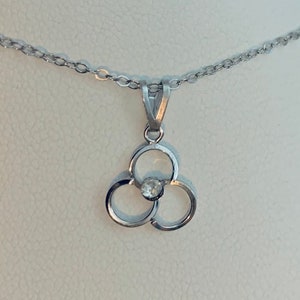 May include: A silver necklace with a pendant in a three-petal design. A small, clear gemstone is set in the centre of the pendant. The necklace chain is also silver and has a delicate link pattern.