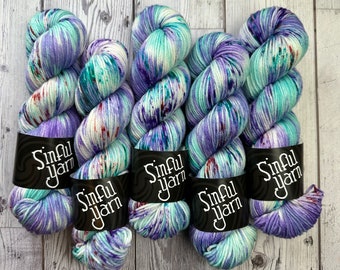 May include: Four skeins of hand-dyed yarn in a purple, teal and white colourway. The yarn is labelled "Sinful Yarn".